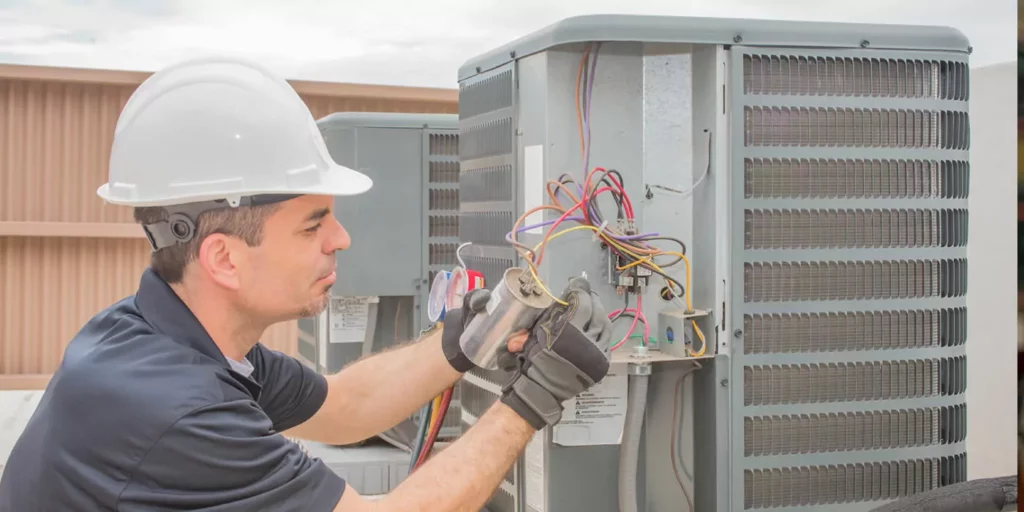 A person with a hard hat works with wires connected to an HVAC unit.