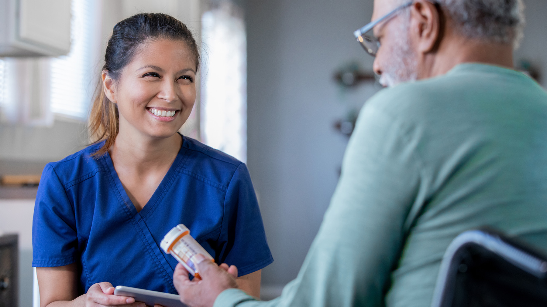 A woman in scrubs smiles at a patient who holds a prescription bottle.